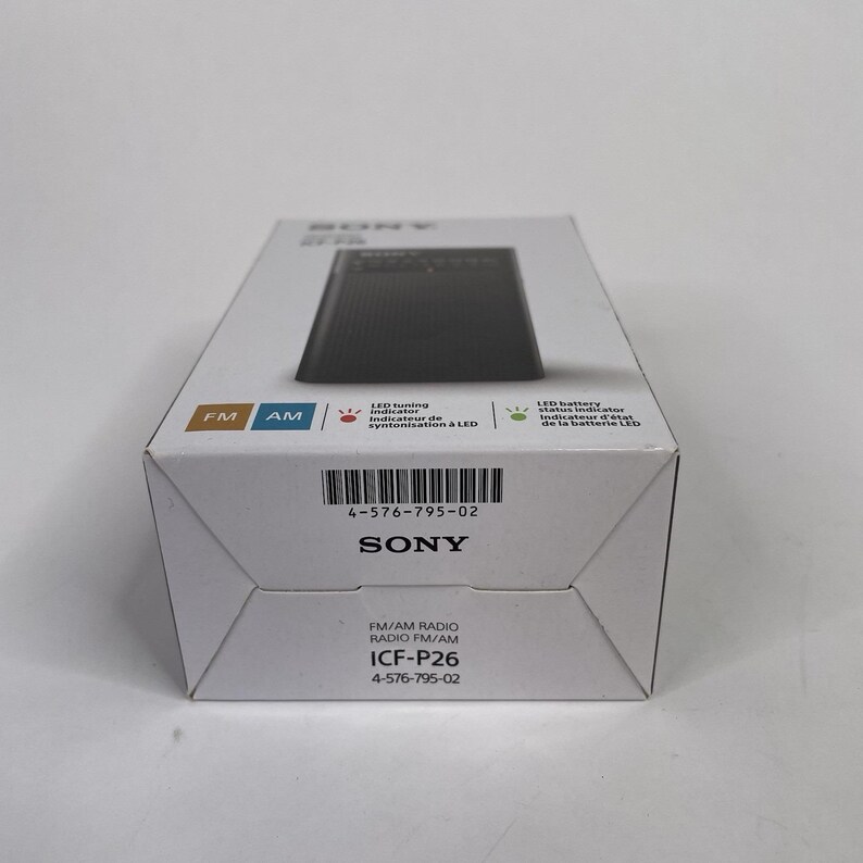May include: A white box featuring a black radio, with the brand name "SONY" and model number "ICF-P26" printed on it. The box also displays "FM" and "AM" indicators, and other text in English and French.