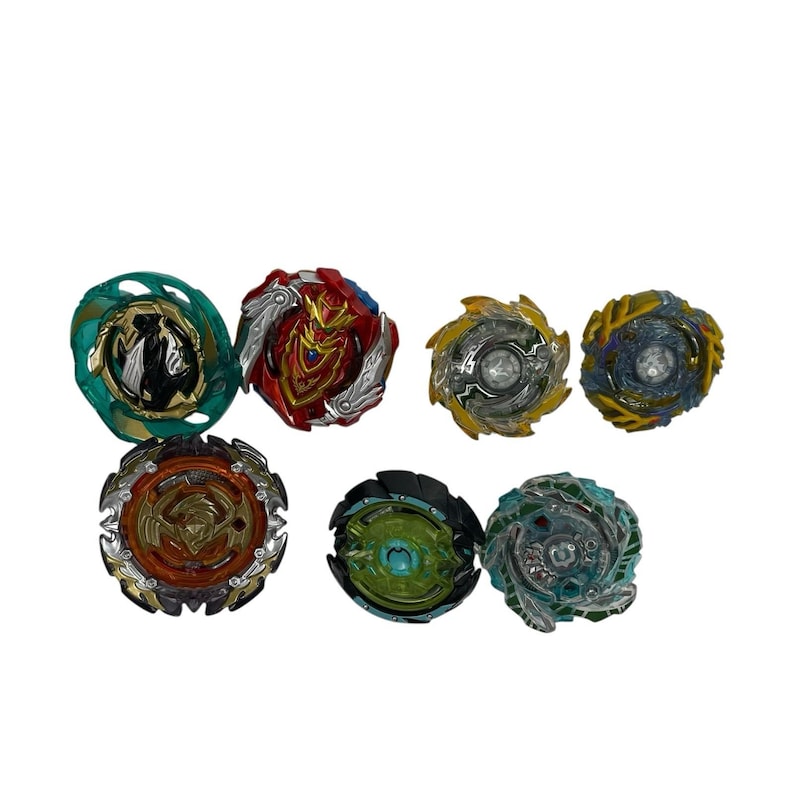 Puede incluir: Una colecci&oacute;n de siete peonzas coloridas. Las peonzas presentan varios dise&ntilde;os y combinaciones de colores, incluyendo verde, rojo, dorado y azul. Est&aacute;n dispuestas sobre un fondo blanco.