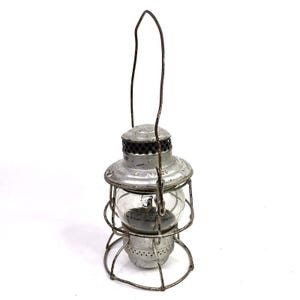 Peut inclure: Lanterne argentée vintage avec un globe en verre transparent et une poignée en fil de fer. La lanterne a une base circulaire et une structure en forme de cage entourant le verre. Le haut de la lanterne a un design décoratif.