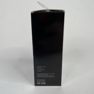 May include: A black rectangular box with the text "Supplied accessory", "Hand strap", "Accessore foun", "Dragonne", "FM/AM RADIO", "ICF-P26". The box has a clear plastic tab extending from the top.