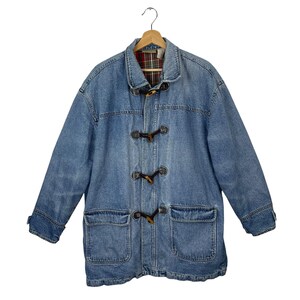 May include: A blue denim jacket with a plaid lining and brown toggle closures. The jacket has two large pockets on the front and a collar.