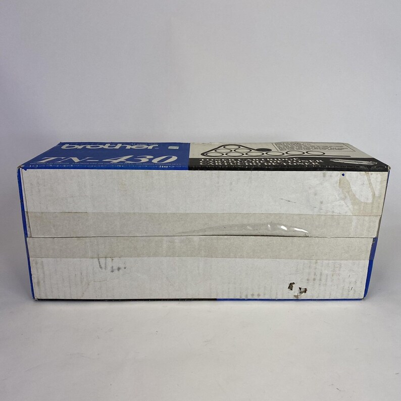 May include: A rectangular box with blue and white panels. The top panel has the brand name "brother" and the model number "TN-430" printed in blue and black. The box is sealed with clear tape and sits on a white surface.