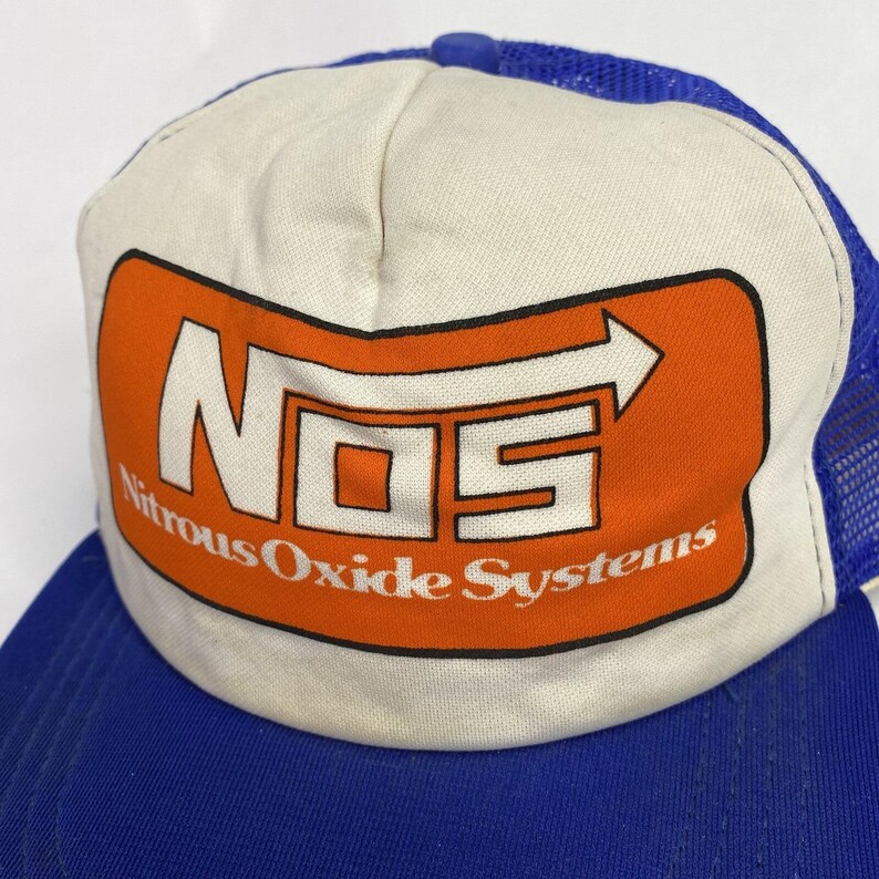 May include: A blue and white trucker hat with the text "NOS Nitrous Oxide Systems" in white and orange. The hat has a mesh back and a curved brim.