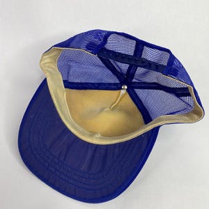 May include: A blue trucker hat with a mesh back and a curved brim. The hat features a snapback closure for adjustable sizing. The interior is lined with a yellow fabric, and the brim is a solid blue color.
