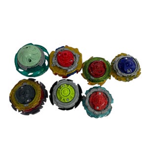 Puede incluir: Una colecci&oacute;n de siete peonzas coloridas. Cada peonza presenta un dise&ntilde;o &uacute;nico con varios colores, incluyendo rojo, verde, azul, amarillo y gris. Las peonzas est&aacute;n hechas de pl&aacute;stico y metal, y est&aacute;n dise&ntilde;adas para jugar.