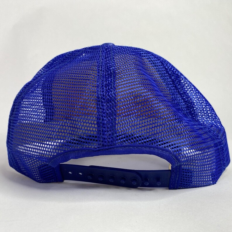 May include: A blue trucker hat with a mesh back and a curved brim. The hat features a snapback closure for adjustable sizing. The mesh is a lighter shade of blue than the front of the hat.