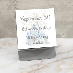 May include: A white card with a watercolor illustration of Cinderella's castle with fireworks. The text reads "September 30, 20 weeks 6 days Until Our Family Vacation!"