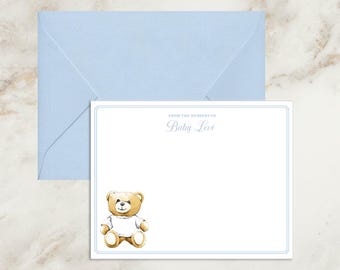 May include: A light blue envelope paired with a white rectangular stationery card featuring a thin blue border. The card displays the text FROM THE NURSERY OF Baby Levi in blue ink and a watercolor illustration of a brown teddy bear wearing a white shirt.