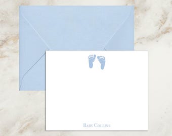 May include: A white rectangular note card with a light blue baby footprint graphic at the top center and the text Baby Collins printed in light blue at the bottom, accompanied by a matching light blue envelope positioned behind the card.