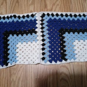 May include: A crocheted blanket with a geometric pattern in white, blue and black.