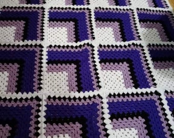 May include: A crocheted blanket with a geometric pattern in shades of purple, white and black.