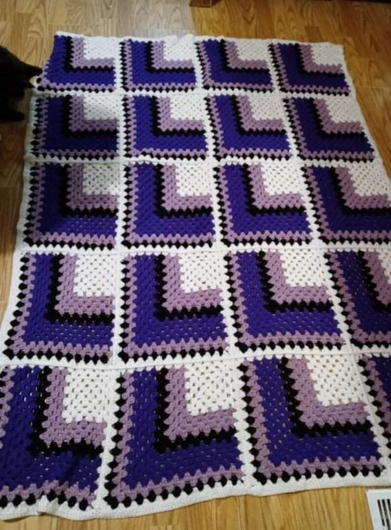 May include: A crocheted blanket with a geometric pattern in shades of purple, black, and white.