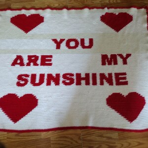 May include: White crocheted blanket with red hearts and the text "You are my sunshine" in red.