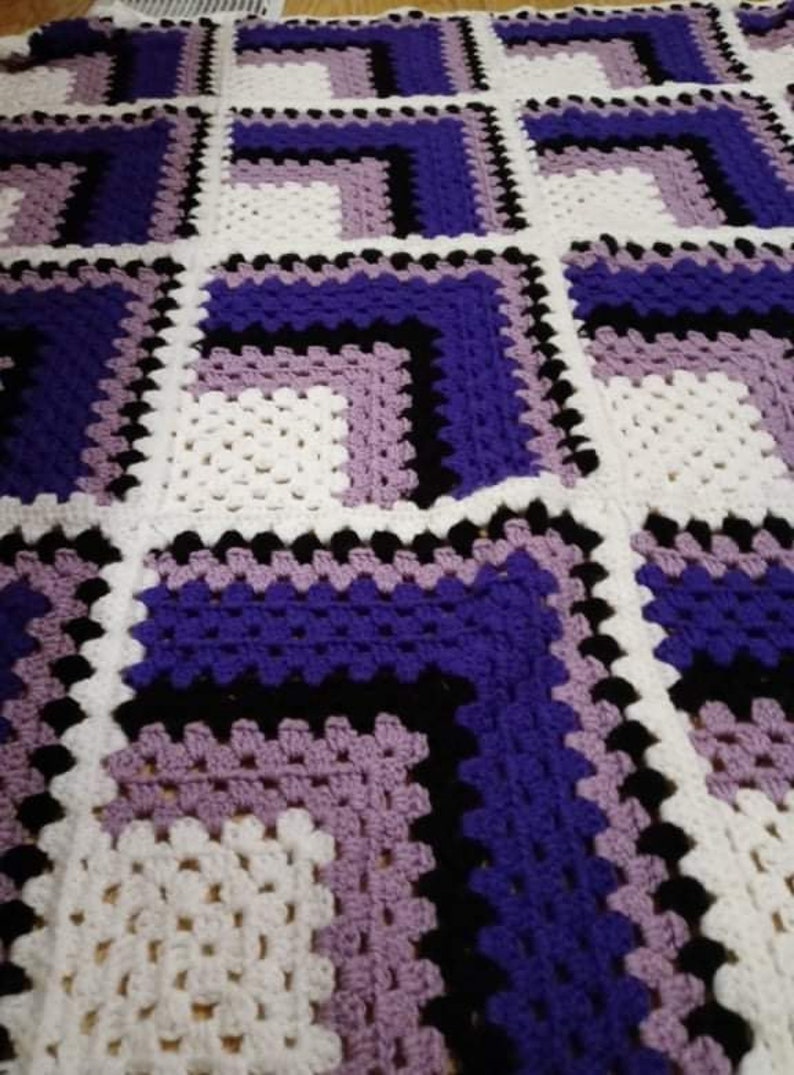 May include: A crocheted blanket with a geometric pattern in shades of purple, lavender, black, and white.