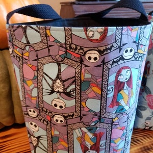May include: A black canvas tote bag with a Nightmare Before Christmas print. The print features Jack Skellington and Sally in a stained glass style. The bag has black handles.