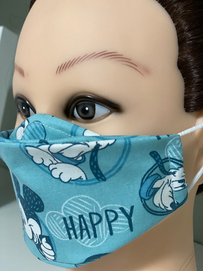 May include: A light blue face mask with a repeating pattern of a cartoon character and the word "HAPPY" in white. The mask has white elastic ear loops.