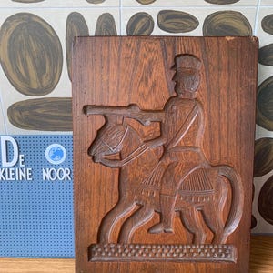 Könnte beinhalten: Ein Holz-Ausstecher in Form einer Person, die auf einem Pferd reitet. Der Ausstecher ist mit komplizierten Details geschnitzt und hat eine dunkelbraune Farbe.