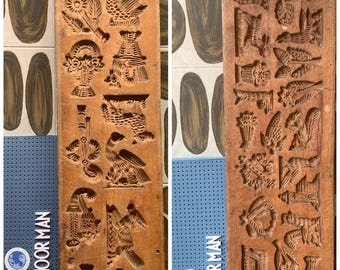 May include: Two antique wooden cookie molds with various carved designs, including birds, flowers, and figures. The molds are rectangular and feature detailed relief carvings. The wood has a warm, natural tone, and the molds are displayed against a patterned background.