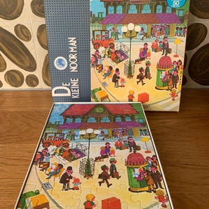 May include: A vintage King Puzzle box with a colorful illustration of a train station scene. The box is blue and white with the text "De Kleine Noorman" on the front. The puzzle is 50 pieces.
