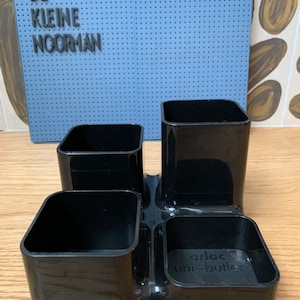 May include: Black plastic desk organiser with four compartments. The organiser has the text "arlac uni-butler" on the bottom.