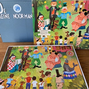 May include: A vintage jumbo puzzle box with a colorful illustration of clowns, animals, and people. The box is blue and white with the text "De Kleine Noor Man" and "jumbo puzzle 50 pieces".