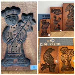 May include: Four wooden cookie cutters, two with figures of people holding a branch, one with a bird, and one with a person holding a branch. The cookie cutters are all brown and have a worn look. The text "DE KLINE NOOR MAN" is visible on one of the cookie cutters.