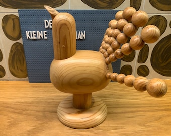 May include: A wooden bird sculpture with a rounded body and a long, beaded tail. The bird is standing on a round base.