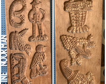 Op de afbeelding: Twee antieke houten koekvormen met gesneden ontwerpen. Eén vorm heeft een figuur van een man, een vogel en andere vormen. De tweede vorm heeft een mand, een draak en andere vormen. De vormen zijn van hout en hebben een warme, bruine kleur.