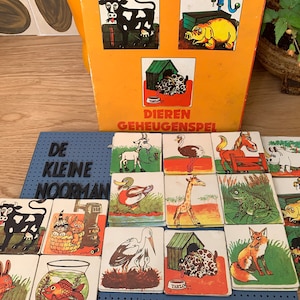 Puede incluir: Un tablero de juego azul y blanco con el texto "De Kleine Noorman" y 16 tarjetas de imágenes coloridas que representan animales, una rana, un pájaro y un pez. Las tarjetas están dispuestas en una cuadrícula. El tablero de juego está hecho de cartón y tiene un marco de madera.