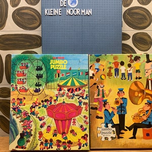 May include: Two vintage jumbo jigsaw puzzles. The first puzzle depicts a colourful amusement park scene with a Ferris wheel, carousel, and many people. The second puzzle shows a band of musicians playing instruments in a park setting. Both puzzles are 100 pieces.