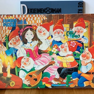 May include: A vintage jumbo puzzle featuring a princess and seven dwarfs. The princess is wearing a pink dress and a red bodice. The dwarfs are wearing red hats and colorful clothing. The puzzle is set in a whimsical forest scene with a wooden house in the background.