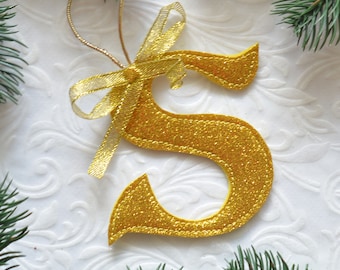 May include: Gold glitter letter S Christmas ornament with a gold ribbon bow.