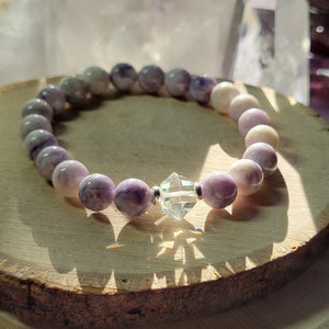 May include: A purple and white gemstone bracelet with a clear crystal charm. The bracelet is made of round beads and is strung on elastic.