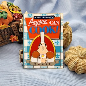 May include: A rectangular pin featuring a chef with the text "Anyone Can Cook!" in red and blue. The pin has a blue and white tile pattern background and gold accents. The chef is wearing a white hat and holding a medal.