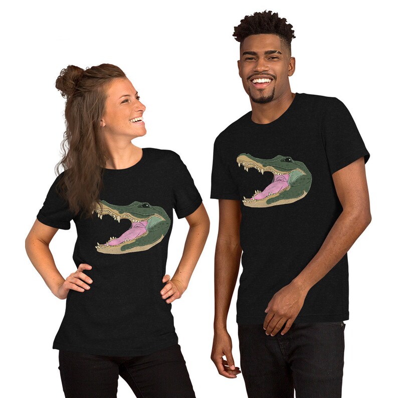 May include: Two people wearing black t-shirts with a graphic print of an alligator's head with its mouth open. The alligator is green with a pink tongue.