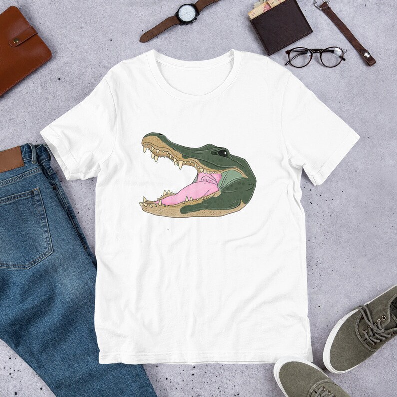 May include: White t-shirt with a green alligator head graphic. The alligator's mouth is open, revealing its teeth and pink tongue.