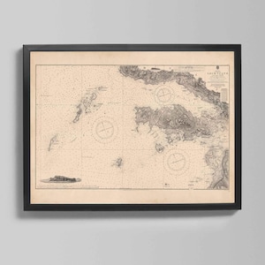 May include: A framed vintage nautical chart, featuring detailed coastlines and sea depths. The map is in black and white, with intricate lines and shading. The frame is black, and the chart is displayed on a neutral background.