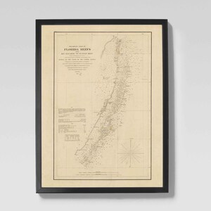 Op de afbeelding: Ingelijste vintage kaart van Florida Reefs met gedetailleerde nautische kaarten en tekst. De kaart is gedrukt op verouderd papier en ingesloten in een zwart frame. Een kompasroos is zichtbaar in de rechter benedenhoek. Historische nautische kaart.