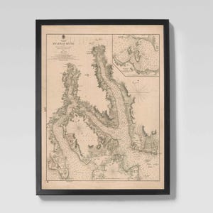 May include: Framed vintage map print of the 'Ayles of Bute' in Scotland. The map shows detailed coastlines, waterways, and geographical features in beige and brown tones. The map is encased in a black frame, suitable for home decor.