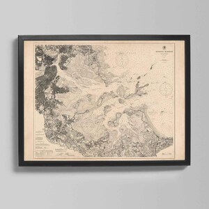 May include: Framed vintage nautical chart of Boston Harbor, featuring detailed coastlines, waterways, and navigational markers. The map is printed in black and white, encased in a black frame, and mounted on a neutral background.
