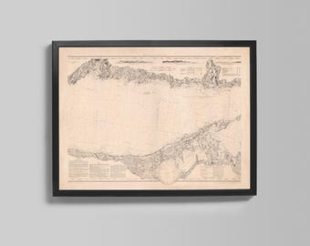 May include: Framed vintage nautical chart with a black frame. The chart features detailed illustrations of coastlines, depths, and navigational information. The map is printed on aged paper, giving it a classic, antique aesthetic. The frame is rectangular and mounted on a gray wall.