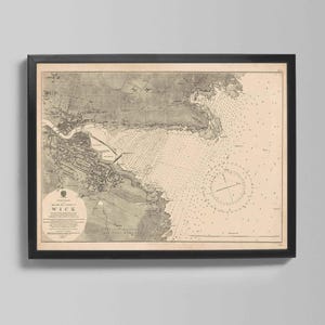 May include: Framed vintage map of Wick, Scotland, in sepia tones. The map features detailed illustrations of the coastline, town, and surrounding waters. The map is enclosed in a black frame, suitable for home or office decor.