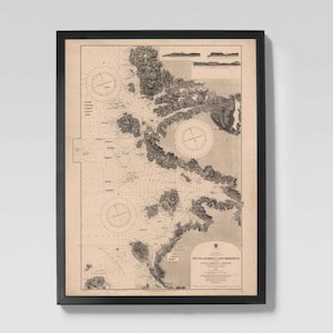 May include: Framed vintage nautical chart with black frame. The map features detailed illustrations of coastlines, islands, and navigational markers. The chart is printed in sepia tones, with compass roses and text. A classic piece of wall art.