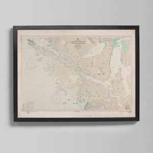 Może przedstawiać: Oprawiona, zabytkowa mapa morska w czarnej ramie. Mapa zawiera szczegółowe ilustracje linii brzegowych, dróg wodnych i elementów nawigacyjnych w odcieniach beżu, zieleni i bieli. U góry widnieje napis "LAND SURVEY TO THE NEW ESTRECHO DE MAGALLANES."