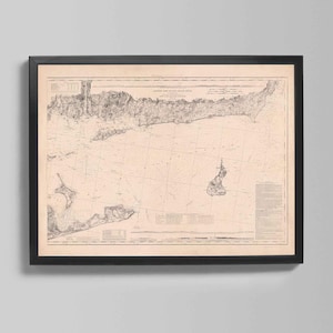 May include: Framed vintage nautical chart of a coastal area, featuring detailed land and sea contours in sepia tones. The chart is enclosed in a black frame, suitable for wall decor. The map includes text and lines indicating depth and geographical features.