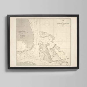 May include: A framed vintage nautical chart of the Atlantic Coast, showing detailed coastlines and navigational data. Printed in grey and beige tones, the chart is presented in a black frame, ideal for maritime-themed interiors.