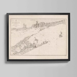 May include: Framed vintage map of Long Island Sound, with detailed coastlines and navigational markers. The map is printed in black and white, framed in a black wooden frame. The map includes text at the top left corner.