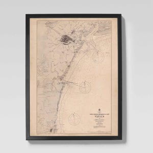 May include: Framed vintage nautical chart of Venice, Italy, in a black frame. The map features detailed coastlines, depth soundings, and navigational markers. The chart is printed on aged paper, giving it a classic, antique aesthetic.