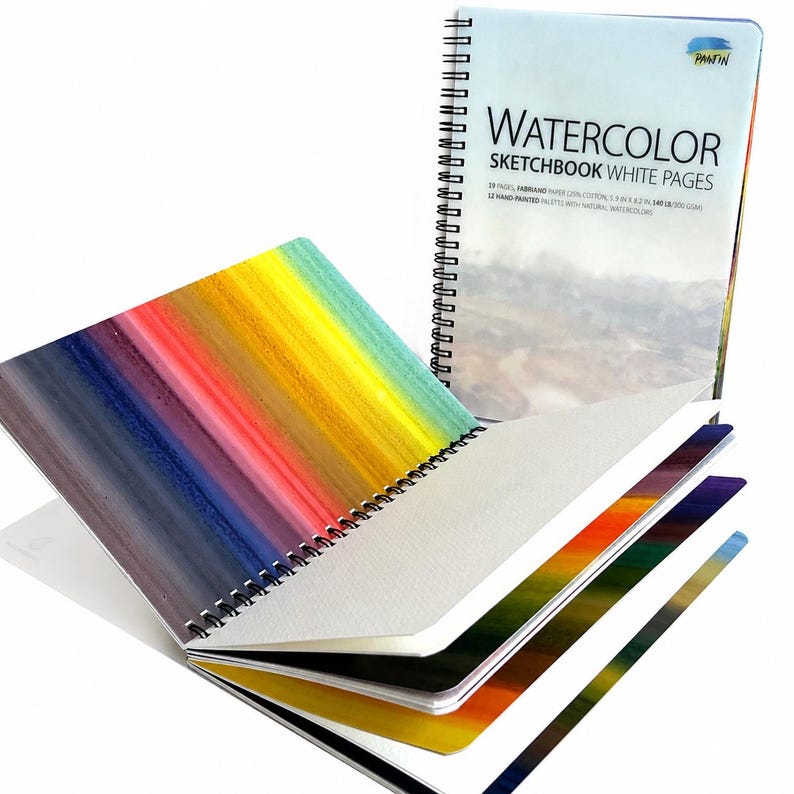 May include: A spiral-bound watercolor sketchbook with white pages, featuring a cover labeled "WATERCOLOR SKETCHBOOK WHITE PAGES" and "PANTIN". The open pages display a vibrant, multi-colored gradient of vertical stripes, including blue, purple, red, orange, and yellow.