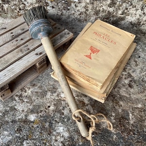 May include: A wooden pallet, a long-handled round brush with dark bristles, and a stack of vintage books with the title LES MIRACLES printed in red on the cover. The books feature a red chalice illustration and aged, off-white paper pages.